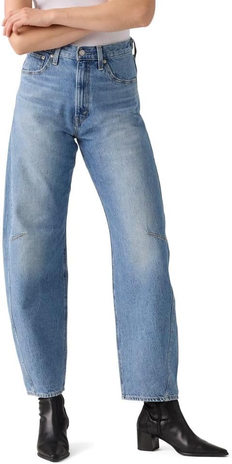 High-waisted medium blue barrel-leg jeans with a relaxed, tapered silhouette, worn with black ankle boots. Features visible fading at thighs and knees, zip fly, and a cropped ankle length.